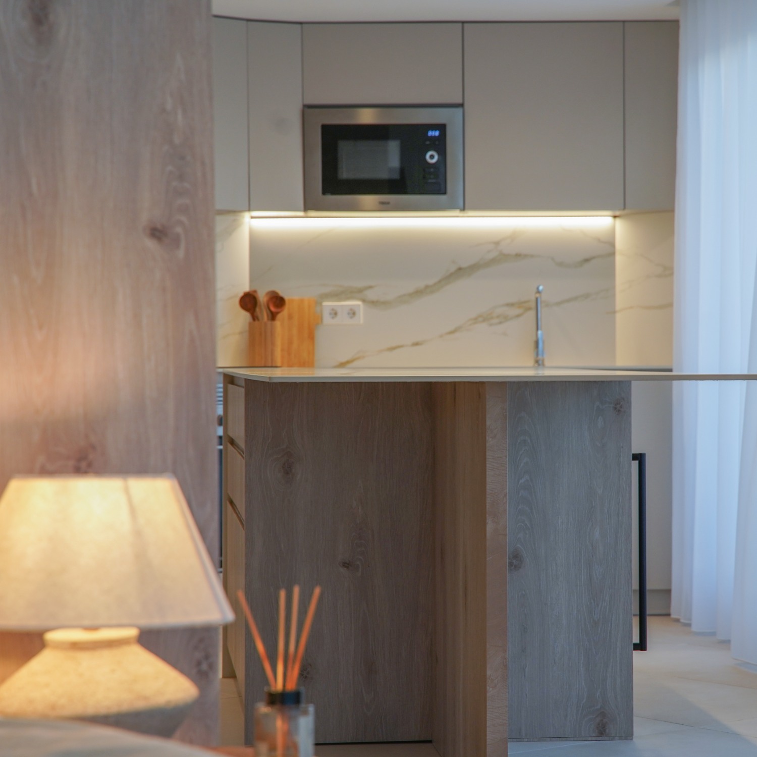 Cocina con panel de madera, encimera de mármol y luz cálida de sobremesa